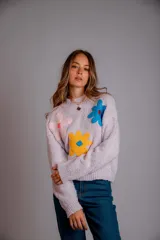 Buzo de punto color lila, con cuello redondo, mangas largas y diseño holgado. Presenta tres flores bordadas en el frente: una rosa claro, una azul y una amarilla con centro azul.