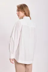 Camisa celeste a rayas verticales, con cuello clásico, cierre frontal con botones, mangas largas abullonadas y corte asimétrico.