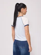 Remera azul marino de algodón con mangas cortas raglán blancas con ribete naranja y estampado ovalado con el logo de Rusty en el pecho.