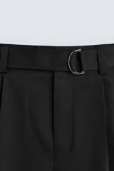 Pantalón negro de corte amplio con cinturón de tela con hebilla metálica. Presenta pliegues frontales, bolsillos laterales y traseros. Cierre frontal con cremallera y botón.