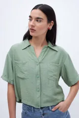 Blusa verde con escote en V, cuello camisero, manga corta y dos bolsillos en el pecho.