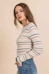 Camiseta tejida rib color beige con rayas horizontales en negro, rosa y marrón. Es de manga larga y cuello redondo.