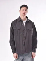 Campera verde militar de mangas largas, con cuello clásico, cierre frontal con botones, dos bolsillos con solapa en el pecho y puños abotonados.