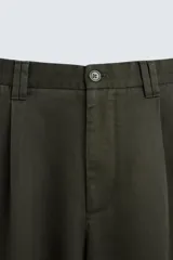 Pantalón verde oscuro de corte amplio confeccionado en tejido de lyocell. Presenta pliegues frontales, bolsillos laterales y traseros de ojal. Cierre frontal con cremallera y botón.