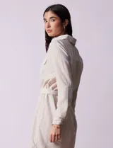Vestido camisero corto a rayas verticales color beige, con cuello con solapa, abertura central con botones, bolsillos aplicados en el pecho y lazo de ajuste en la cintura.