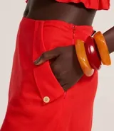 Short pollera de color rojo confeccionado en tejido de viscolino, una mezcla de lino y viscosa. Presenta un diseño de cintura fija con cierre de cremallera lateral y bolsillos frontales con solapa.