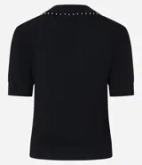 Blusa de punto color blanco, con cuello polo, escote en V y mangas cortas. Detalle de mini perlas aplicadas en el cuello.