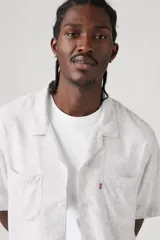 Camisa de manga corta con estampado abstracto en tonos grises y blancos, cuello tipo camp y cierre frontal con botones.