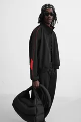 Chaqueta negra con detalles en rojo, cuello alto, cierre frontal con cremallera, bolsillos laterales y puños elásticos.