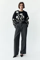 Pantalón negro de tiro alto con pinzas delanteras, pernera ancha y cinturón de cuero con hebilla dorada.