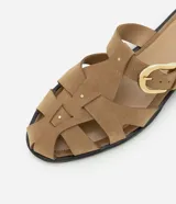Sandalia plana color beige, tipo mule fisherman, con tiras trenzadas, hebilla lateral y suela negra.