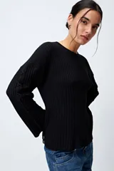 Sweater negro de punto canalé con detalle de trenzado en las mangas y lazo ajustable en el ruedo.
