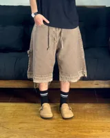 Bermuda de corte baggy color marrón con efecto gastado (lavado vintage), doble carpintero y detalle artesanal visible en el bajo. Incluye un cordón extra confeccionado en la misma tela.