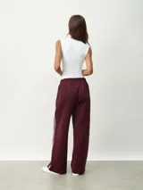 Pantalón deportivo color borgoña, de corte ancho y cintura elástica. Presenta una franja blanca vertical a lo largo de la pierna.