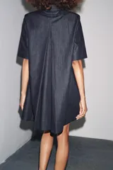 Vestido corto de Zara Woman Collection confeccionado en tejido tipo denim. Tiene cuello solapa, manga corta, bolsillos delanteros ocultos, bajo evasé y cierre frontal con botones.