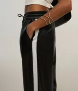 Pantalón pantalona de cuero sintético negro con cintura elástica, lazo ajustable y raya lateral blanca.