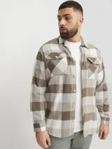 Sobrecamisa a cuadros beige, marrón y blanco, de manga larga y cuello camisero con fit confort. Cierre con botones y bolsillos en el pecho con solapa y broche. Estilo plus size diseñada para cuerpos de talla grande. Tejido de sarga resistente con patrón en “V” característico.