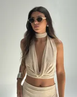 Top sin mangas color beige con diseño drapeado en el escote y cuello alto.