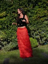 Falda larga color verde oliva con múltiples capas de flecos largos, creando un efecto texturizado. La falda tiene un tajo lateral.