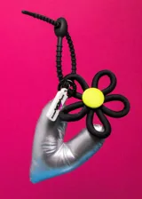 Llavero con dije de corazón plateado, flor negra con centro amarillo y etiqueta blanca con texto negro y rosa.