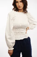 Blusa blanca de algodón con frunces tipo smock en el cuerpo, cuello redondo y mangas largas abullonadas con puños elásticos.