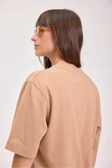 Remera color tostado de algodón con cuello redondo y mangas cortas. Estampado pequeño en el centro del pecho con un sol y texto.