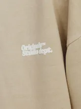 Hoodie color beige con estampado en la espalda con la frase "Originals Studio dept" en letras blancas.