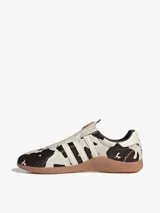 Zapatillas Adidas Taekwondo Mei sin cordones, con capellada de cuero vacuno con estampado animal print de vaca, las tres tiras características de la marca en cuero blanco y suela de goma color caramelo.