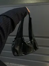 Bolso tipo hobo de cuero negro con tachas plateadas. Tiene cierre con imanes, bolsillo externo con imán y sobre interno con gancho.