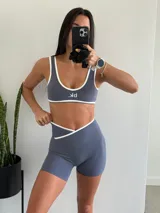 Conjunto deportivo gris con detalles en blanco, compuesto por un top con logo y unos shorts de tiro alto.