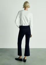Pantalón de jean azul oscuro, de tiro alto, corte crop y acampanado. Cuenta con cierre de cremallera y botón, trabillas, cinco bolsillos y tejido elástico.