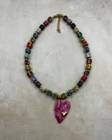 Collar corto compuesto por cuentas cerámicas cuadradas de diferentes colores y esmaltes, separadas por pequeñas cuentas doradas. Cierra con mosquetón dorado y tiene un dije colgante grande en forma de corazón esmaltado en color rosado/fucsia con un pequeño corazón dorado superpuesto.
