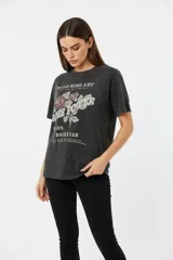 Remera de algodón, color gris oscuro con efecto gastado (acid wash), corte holgado y manga corta. Presenta un estampado frontal con motivos florales y texto en tonos rosados y blancos, incluyendo las frases "WILD ROSE ART", "ROSE POWER", "ST 1978" y "ROCKSTAR".