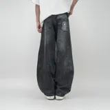 Pantalón de jean negro con lavado oscuro y efecto desgastado, de corte ultra ancho y tiro alto. Presenta un parche circular con logo en el bolsillo trasero derecho.