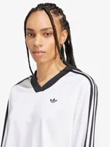 Top corto blanco de manga larga con cuello en V y ribete negro. Presenta las tres rayas características de Adidas en las mangas y el logo bordado en el pecho.