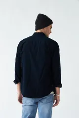 Camisa de pana color verde militar, de corte regular, con cuello clásico y cierre frontal con botones.