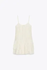 Vestido corto color crudo, de gasa, con escote en V y tirantes finos regulables. Presenta cordón cruzado con lazada en el delantero y falda con volantes. Cierre trasero con cremallera oculta.