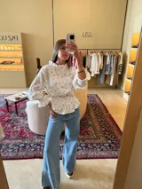 Camisa blanca con estampado de flores pequeñas, cuello con volados, mangas largas abullonadas con puños elásticos y corte peplum.