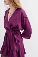 Vestido corto color violeta, de escote cruzado con volados, mangas largas abullonadas y cintura elastizada. Confeccionado en jacquard con corazones.