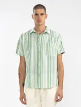 Camisa de manga corta a rayas verticales azules y blancas, con cuello clásico, corte cuadrado y calce relajado. Presenta botones de coco con logo y parche distintivo de Polonio. Confeccionada en Italia con mezcla de lino y algodón.