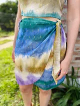 Falda corta cruzada con estampado batik en tonos verde, azul, marrón y lila, con detalles dorados y lazo lateral.