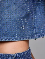 Top corto de denim azul con apliques de strass plateados distribuidos por toda la prenda. Presenta un escote en V y breteles finos, también adornados con strass.