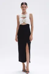 Vestido midi negro y blanco, sin mangas, con top blanco drapeado con bordados florales de tul con perlas y cuentas de vidrio doradas, falda negra con tajo lateral y corte ajustado.