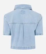 Camisa cropped de jeans celeste con cuello clásico, mangas cortas, cierre frontal con botones y bolsillo en el pecho.