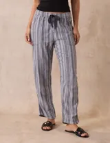 Pantalón largo de lino y rayón a rayas verticales grises y blancas. Tiene pretina elastizada con lazo de ajuste, bolsillos delanteros y traseros.
