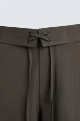 Pantalón marrón de corte ancho, con cintura ajustable con cordón, bolsillos delanteros y traseros tipo parche, detalle de costuras verticales en el frente y cierre frontal con cremallera y gancho metálico oculto.