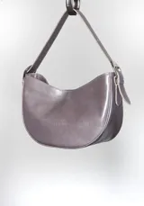 Cartera tipo lady bag color lila, de cuero sintético, con correa ajustable y herrajes metálicos plateados.