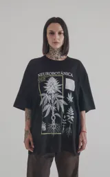 Remera negra de algodón con cuello redondo y calce oversize. Estampado frontal con diseño de plantas y texto 'Neurobotánica: El Código Raíz de la Vida'.