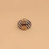 Anillo con cuerpo plateado con rayas diagonales negras y tres bandas de oro en el centro.