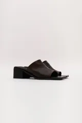 Sandalia marrón de cuero con punta cuadrada, talón abierto y faja ancha. Tiene detalle de elástico oculto en la cara interna de la capellada. El forro y la plantilla son de cuero vacuno.